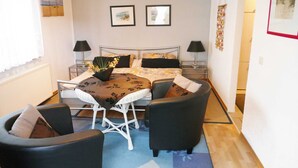 Une chambre à coucher comprenant un lit, deux tables de chevet, une chaise, une petite table et une fenêtre avec des rideaux.