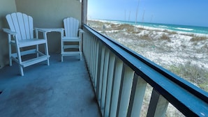 A balcony with two white Adirondack chairs and a small table, overlooking a beach with sand dunes and the ocean. - Fabulous 1BR Condo with amazing beach views sleeps 4. Park by door. Pool. (Panama City Beach)