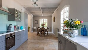 A kitchen with a dining area, featuring a large window, a table with chairs, and a vase with flowers on the counter. - Quiet 50's cottage - 12 p. - Private park & pool (Fourcès)