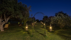 Un jardín nocturno con un sendero, árboles y mobiliario de exterior.