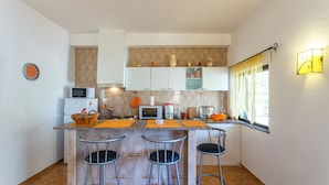 Una cocina moderna con una isla central, taburetes de bar, microondas, tostadora y un reloj en la pared.