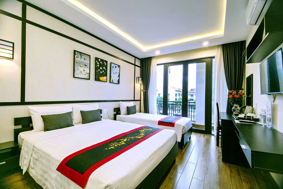 A hotel room with two beds, a desk, and a balcony with a view.