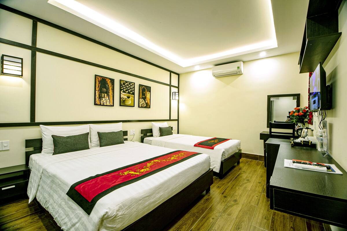 A hotel room with two beds, a desk, a TV, and artwork on the wall.