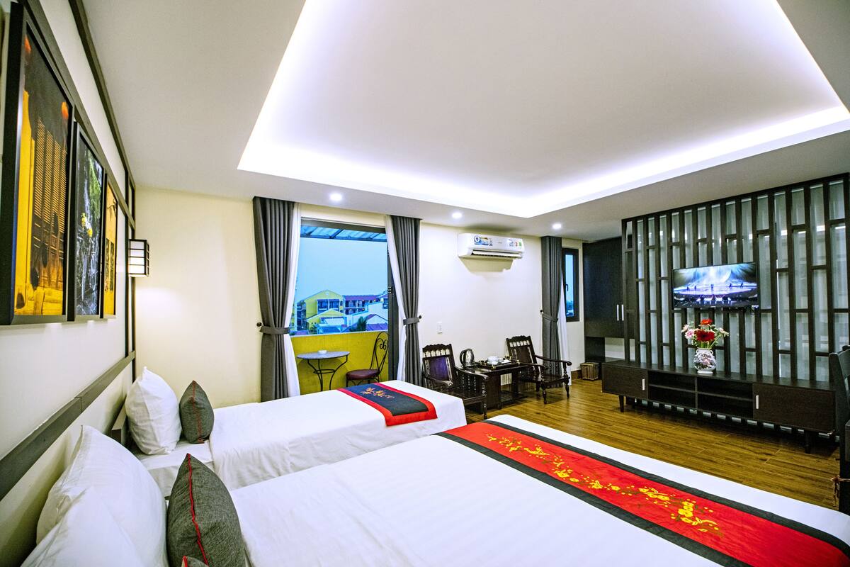 A hotel room with two beds, a TV, a desk, and a balcony with a view.