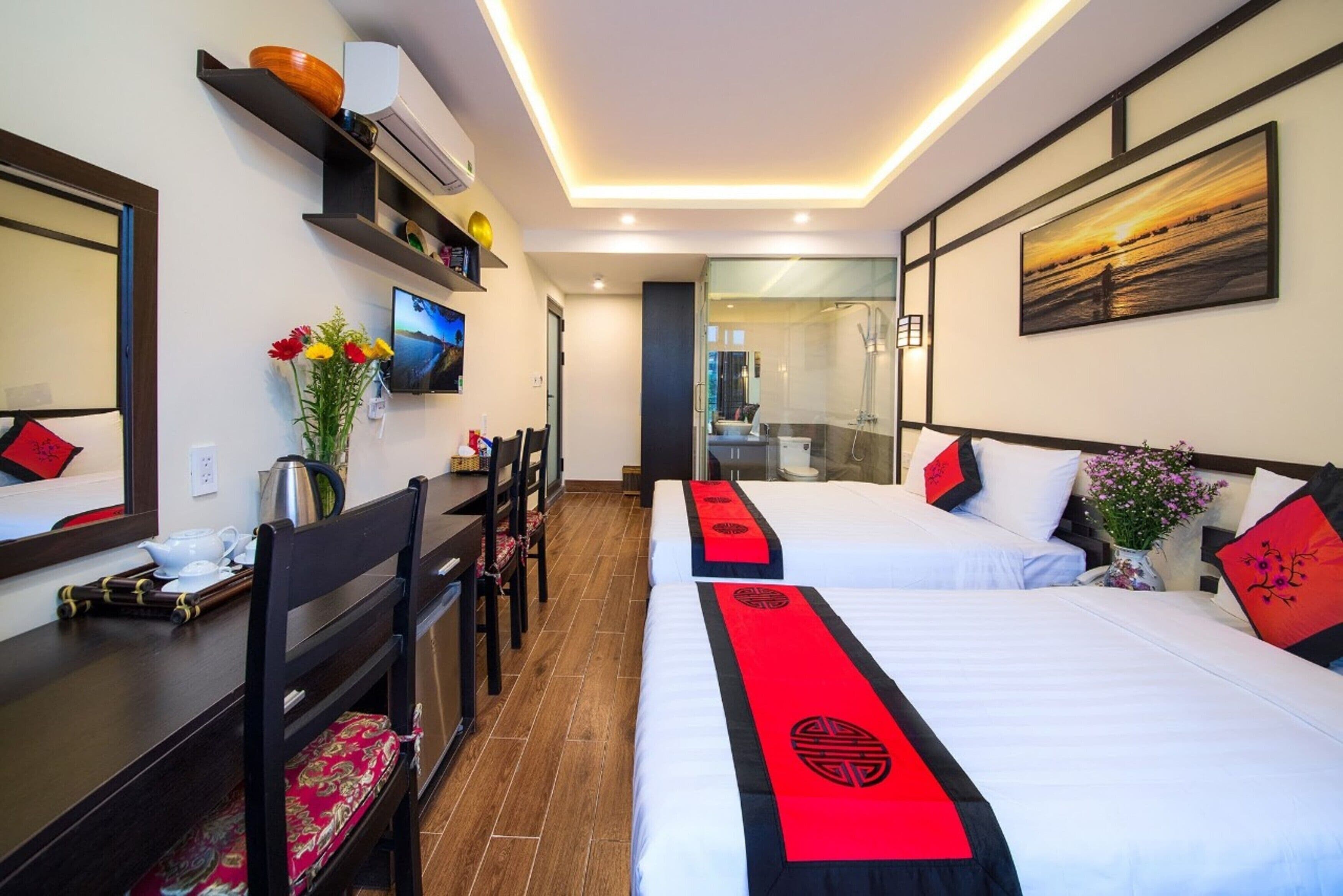 A hotel room with two beds, a desk, a chair, a TV, and a bathroom visible through a glass door.