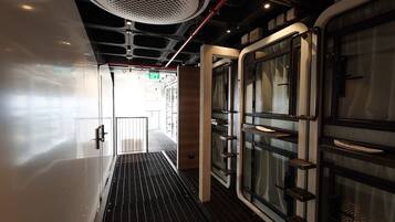 A corridor with a metal grate floor, glass doors, and a ceiling with a circular light fixture.