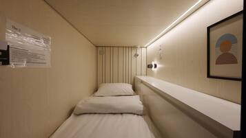 A narrow hotel corridor with a single bed, a wall-mounted light, and a framed picture.