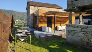 A modern outdoor kitchen with a grill, a stone wall, and a wooden pergola. - A Casa de Costa (Laxe)