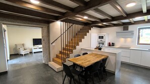 A modern kitchen with a wooden dining table and chairs, a built-in oven, and a staircase leading to another level. - A Casa de Costa (Laxe)