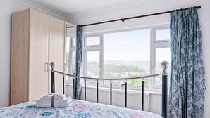 A bedroom with a bed, a wardrobe, and a window with curtains. - Peaceful Home in Looe with Stunning Views (Looe)