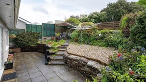 A garden with a stone pathway, a wooden fence, and various plants. - Peaceful Home in Looe with Stunning Views (Looe)