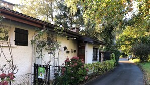A residential street with a house featuring a white facade, a visible garden with pink flowers, and a metal fence. - Gîte LE Petit Renard (Dabo)