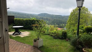 A garden with a paved patio, a table, and a street lamp. - Gîte LE Petit Renard (Dabo)