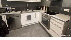 Cozinha moderna com armários brancos, eletrodomésticos de aço inoxidável e painel de azulejos cinza.