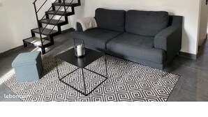 Uma sala de estar moderna com um sofá cinzento, uma escadaria preta e um tapete estampado.