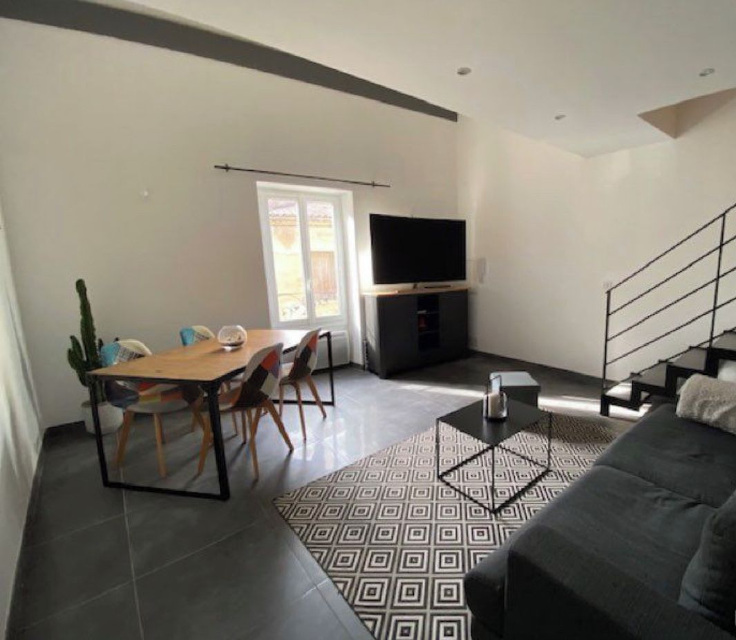 A modern living room with a sofa, a dining table with chairs, a staircase, and a TV.