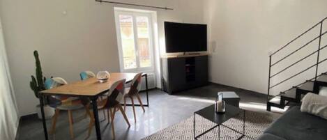 A modern living room with a sofa, a dining table with chairs, a staircase, and a TV.
