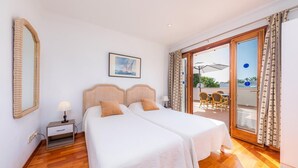 Habitació doble amb dos llits, una tauleta de nit, una làmpada, un quadre amb marc i una porta corredissa de vidre que dona a una zona exterior amb taula i cadires.