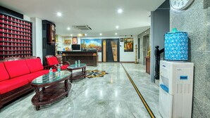 A hotel lobby with a red sofa, a wooden coffee table, a water dispenser, and a clock on the wall. - Corbelli Residency  (Puducherry)