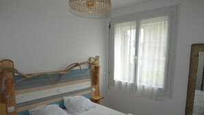 A bedroom with a wooden headboard, a bed with white bedding, a window with sheer curtains, and a mirror on the wall. - 2-Bedroom Apartment in City Center with Terrace and Private Parking in Royan (Royan)