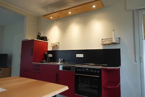 A compact kitchen with red cabinets, a black countertop, and a built-in oven.