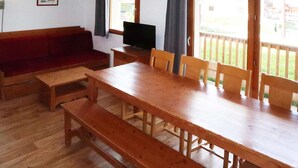 A wooden dining table with benches, a red sofa, a television, and large windows with curtains.