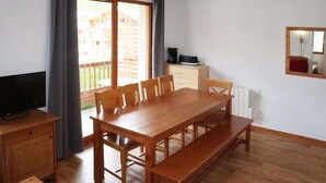 A dining area with a wooden table and benches, a television on a stand, and a view of a wooden deck outside.