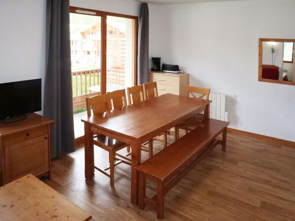 Un comedor con una mesa de madera y bancos, un televisor sobre un mueble bajo, y vista a una terraza de madera.