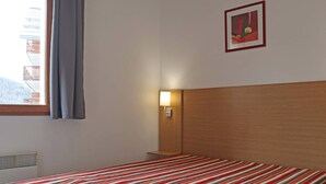 A hotel room with a bed, a nightstand, a wall-mounted lamp, and a window with curtains.