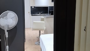 A room with a bed, a white fan, a small kitchenette, and a white chair. - Budget Ensuite Room in Thamesmead (London)