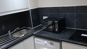 A compact kitchen with a washing machine, a microwave, and a sink. - Budget Ensuite Room in Thamesmead (London)
