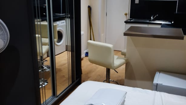A hotel room with a bed, a chair, a TV, a small kitchen area, and a washing machine. - Budget Ensuite Room in Thamesmead (London)