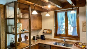 Een keuken met houten kastjes, een inbouwkast, een dubbele spoelbak en een raam met gordijnen.