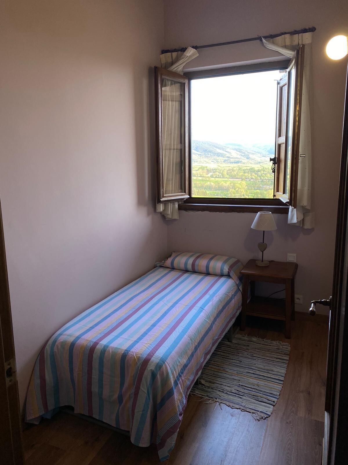 A small, single-bed room with a window overlooking a landscape.