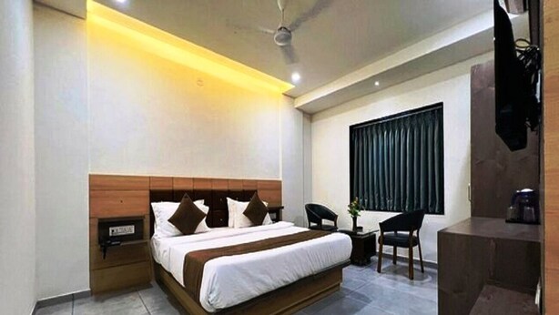 A modern bedroom with a large bed, bedside tables, a chair, and a small table. - Hotel Venus (Ootacamund)
