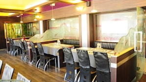 A restaurant with booths and high tables, wooden flooring, and a decorative wall with bamboo artwork. - Hotel Venus (Ootacamund)