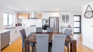 Eine moderne Küche mit weißen Schränken, einem Edelstahl-Kühlschrank und einem Essbereich mit Holztisch und grauen Stühlen.