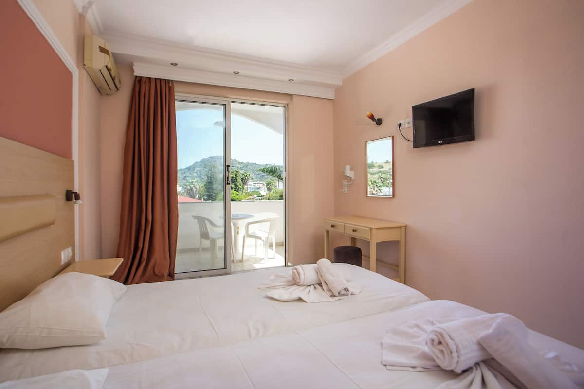 A hotel room with a bed, a television, a desk, and a sliding glass door leading to a balcony.