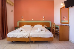 A double bed with white linens, a wooden desk, a chair, and a television mounted on the wall. - Diagoras Hotel (Rhodes)