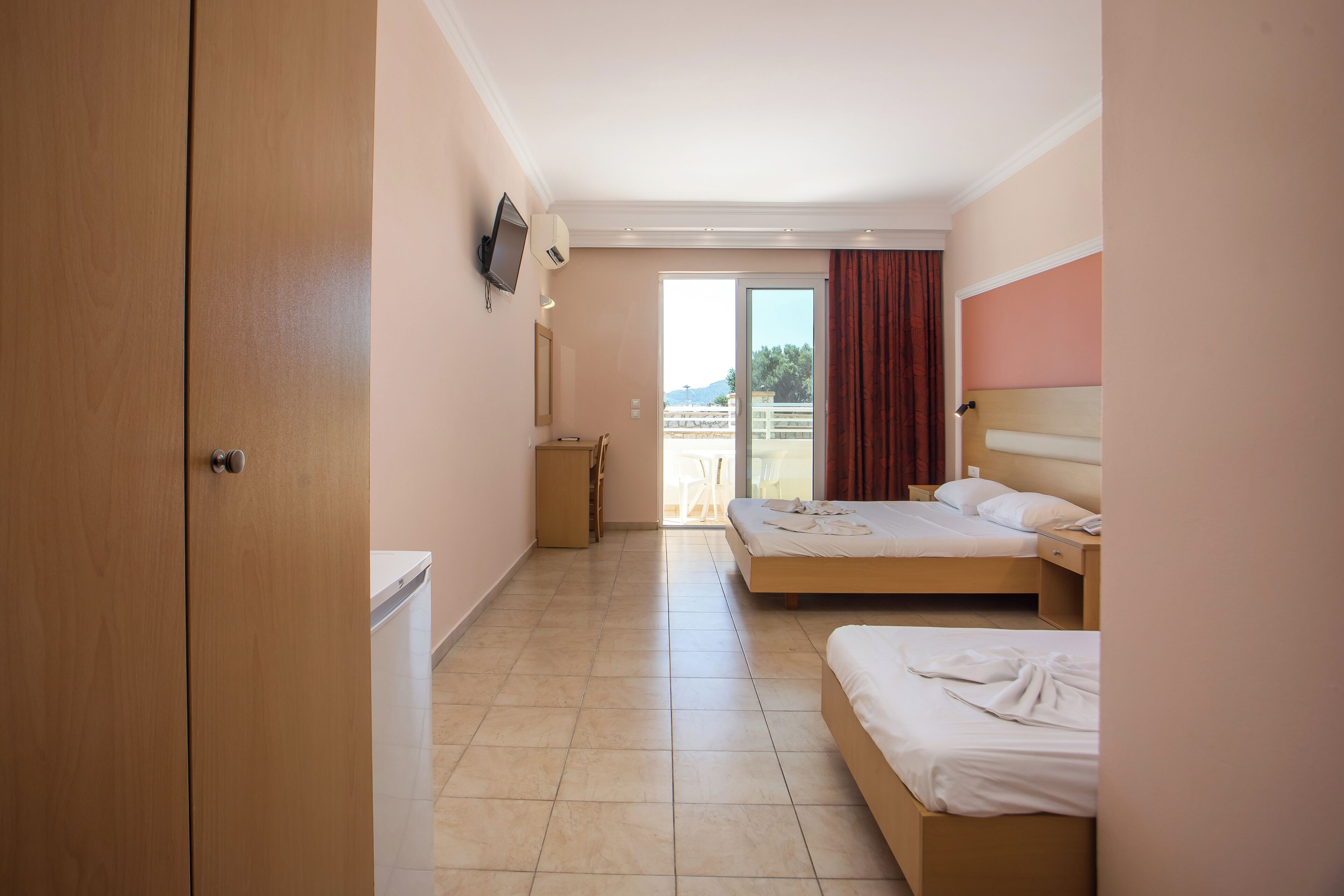 A hotel room with two beds, a TV, a small table, and a view of the outdoors.