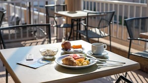 A table with breakfast items, a cup, and a smartphone on a balcony with chairs and a railing. - Diagoras Hotel (Rhodes)