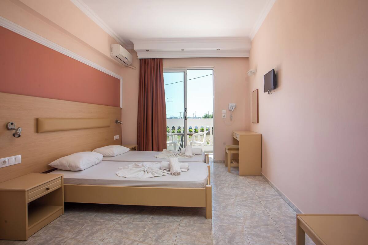 A hotel room with a bed, bedside table, a desk, a chair, a TV, and a balcony with a view.