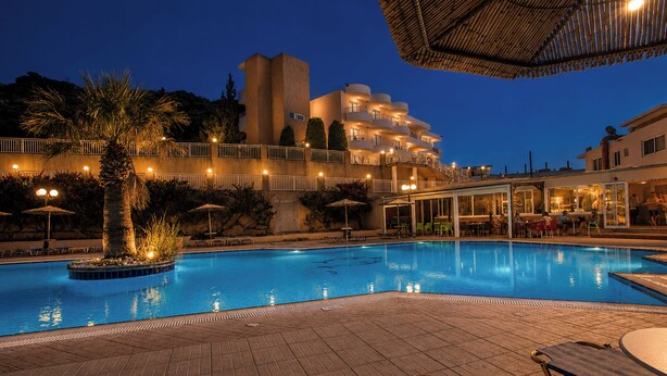 A swimming pool with lounge chairs, a palm tree, and a building with balconies in the background. - Diagoras Hotel (Rhodes)