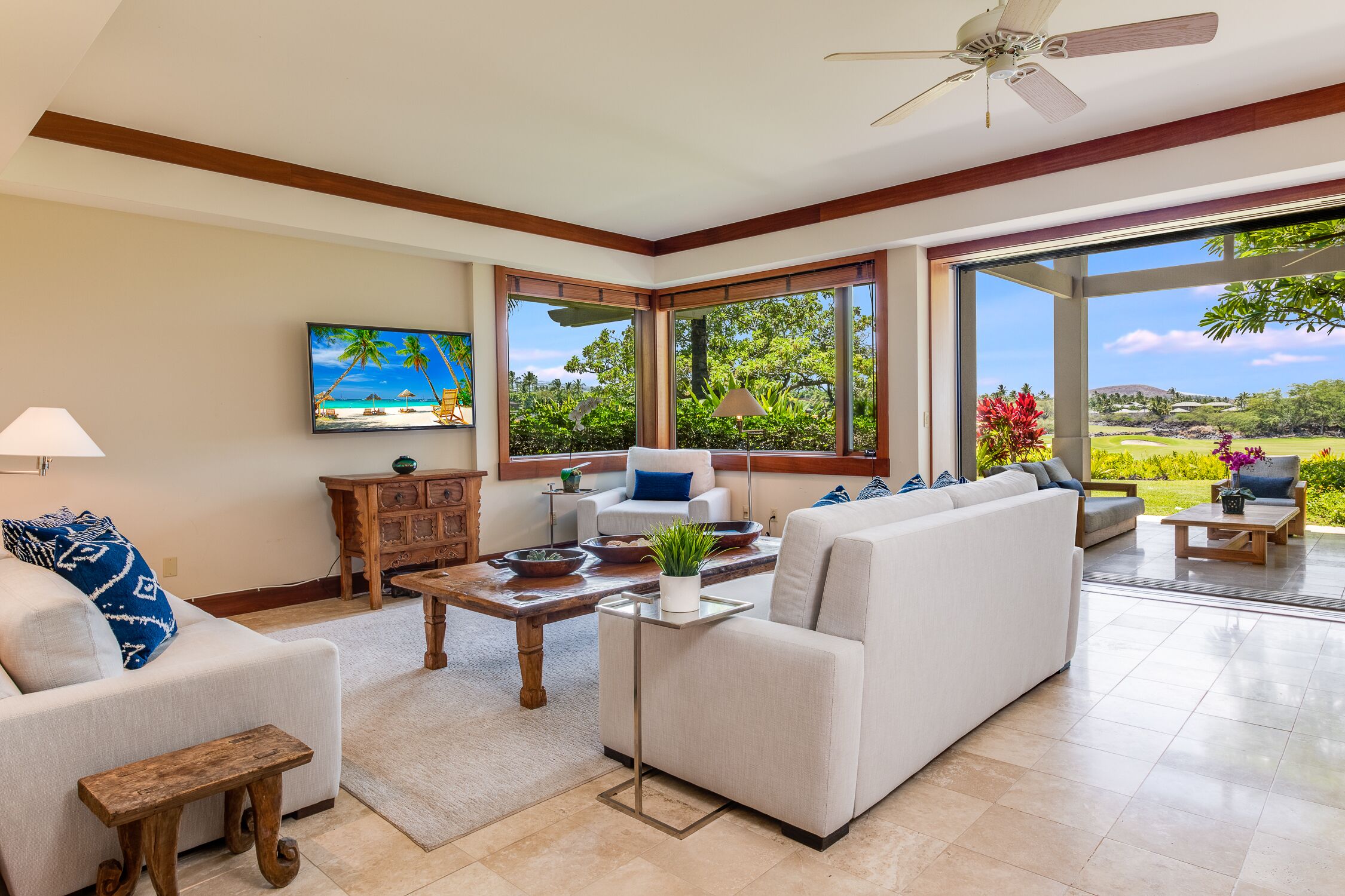 A spacious living room with a large window, a ceiling fan, and a painting of a beach scene.