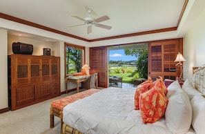 Ein Schlafzimmer mit einem großen Bett, einem Holzschrank, einem Schreibtisch mit Stuhl und Blick auf einen Garten durch geöffnete Fensterläden.
