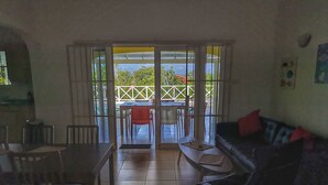 Un salon comprenant un coin repas, un canapé et donnant, grâce à des portes vitrées, sur un espace extérieur aménagé avec des chaises.