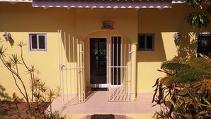Un bâtiment jaune avec un toit recouvert de tuiles rouges, une entrée fermée par un portail et de petites fenêtres.