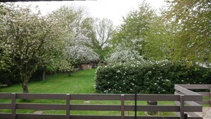 A view from a covered area with a wooden bench in the foreground, a grassy area with blooming trees, and a wooden structure in the background. - Landliebeehrsen 2, modern, quiet location, parking lot.  (Bad Salzuflen)