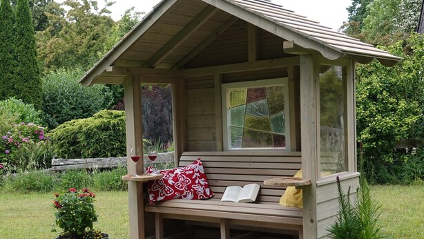 A wooden gazebo with a bench, two potted plants, and a book on the bench. - Landliebeehrsen 2, modern, quiet location, parking lot.  (Bad Salzuflen)