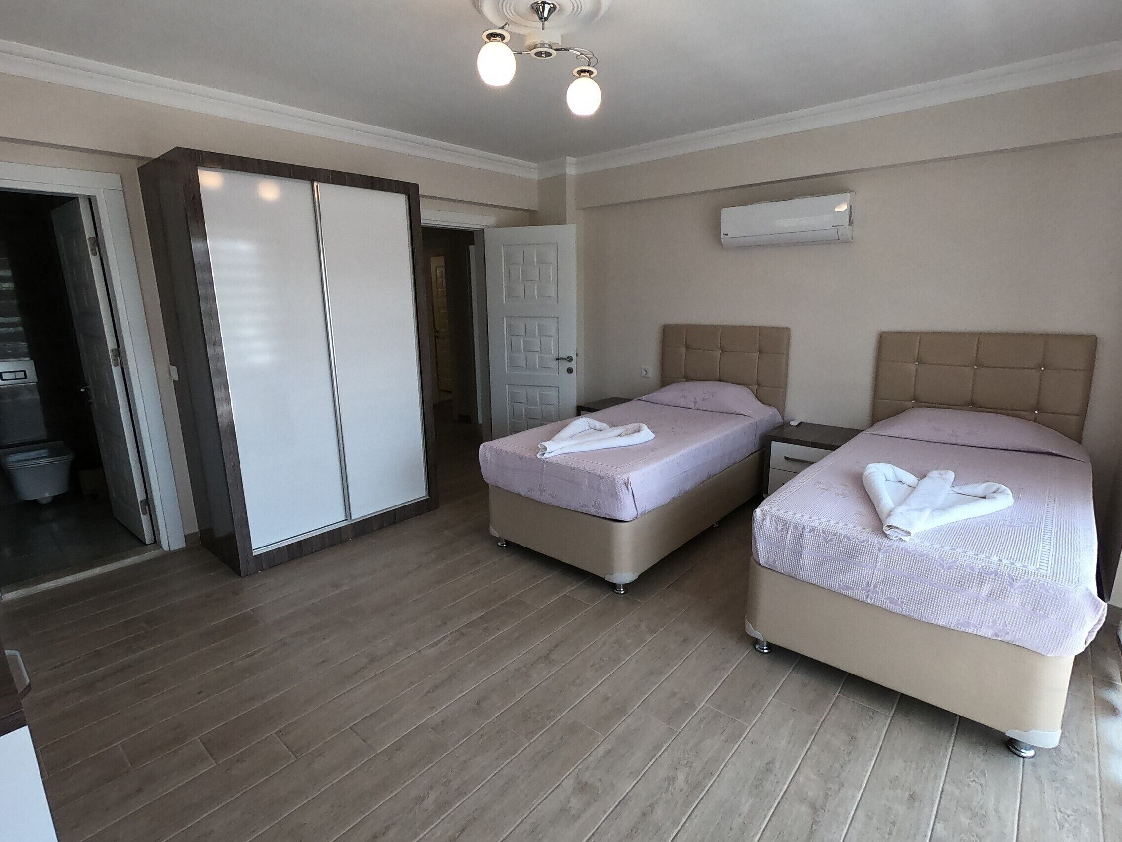 Ein Hotelzimmer mit zwei Betten, einem Schrank, einer Deckenleuchte und einer Klimaanlage.